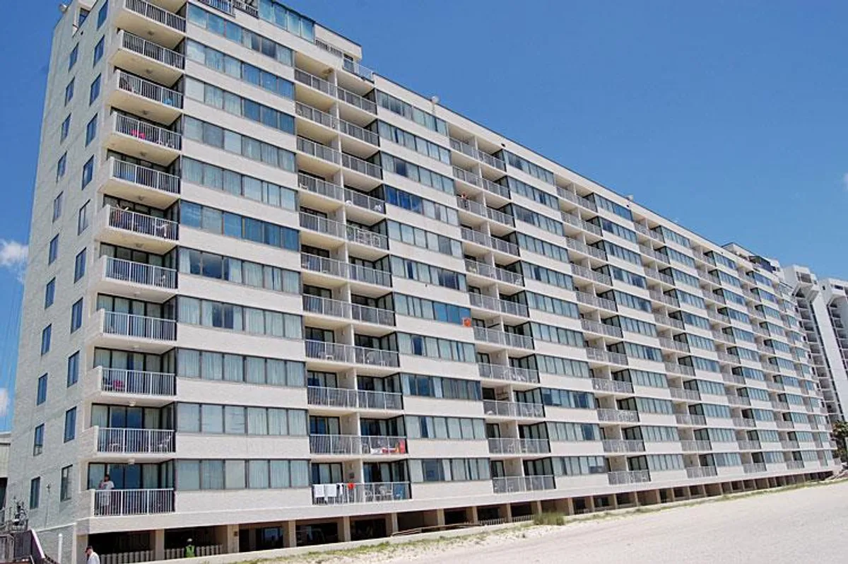 This image captures the exterior of Sands Beach Club, with a focus on the building's modern balconies and expansive windows. The composition hints at private outdoor spaces perfect for enjoying oceanfront views, as palm trees frame the welcoming architecture.