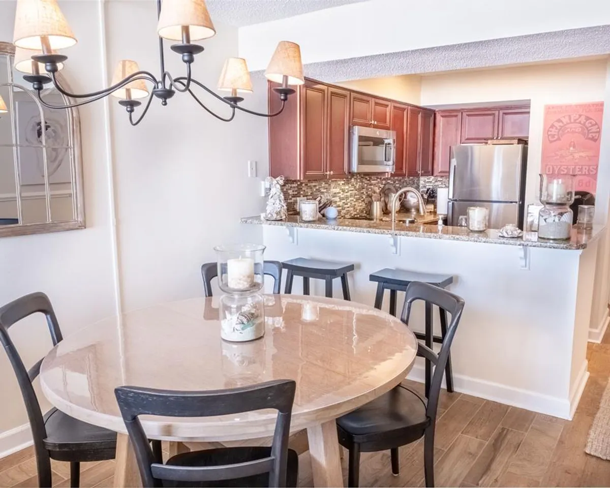 A round dining table sits adjacent to an open kitchen area, illuminated by a chandelier. There are decorative items on the countertop, reinforcing the connection between the kitchen and dining spaces for family meals and casual gatherings.