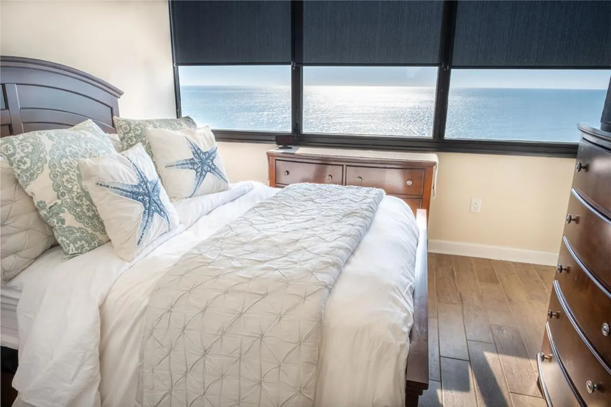 A bright, serene bedroom featuring a comfortable bed adorned with starfish-themed pillows, a soft bedspread, and a window offering a calming view. The scene radiates tranquility and comfort, ideal for unwinding after a day at the beach.