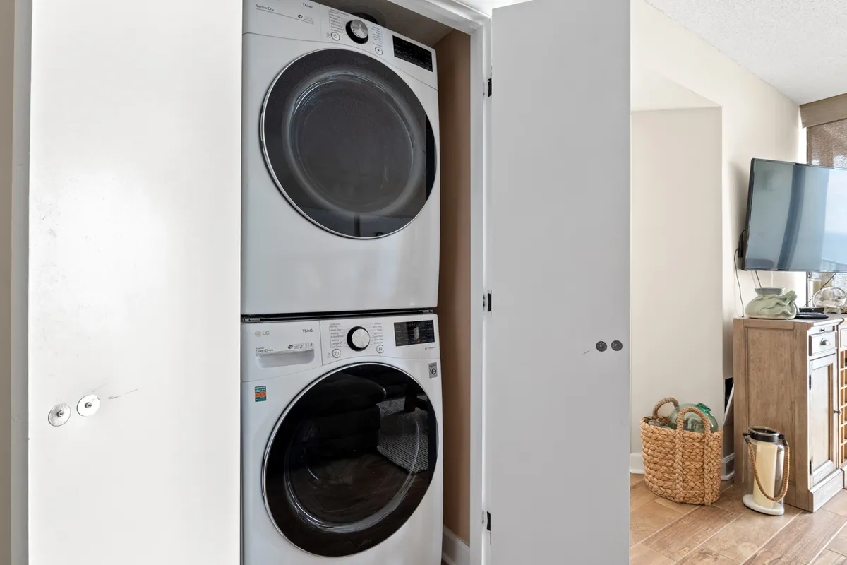 A practical laundry area with a modern stacked washer and dryer, open cupboard doors, and an organized, efficient layout. The scene conveys everyday convenience and a well-maintained space for handling laundry needs, especially after beach outings.