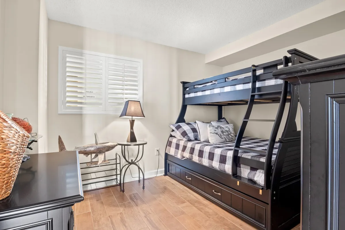 A playful and inviting kids’ bedroom showcasing a bunk (pyramid) bed with checkerboard bedding, a decorative lamp, and a woven basket. The space is designed for versatility, ideal for families or groups, and evokes a sense of coziness and fun.